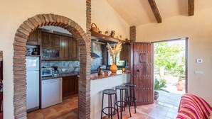 A kitchen with wooden cabinets, a brick archway, a built-in oven, and a bar area with stools. - Villa Calena Almuñécar by Ruralidays (Granada)