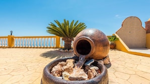 A water feature with a large pot pouring water into a basin surrounded by rocks. - Villa Calena Almuñécar by Ruralidays (Granada)