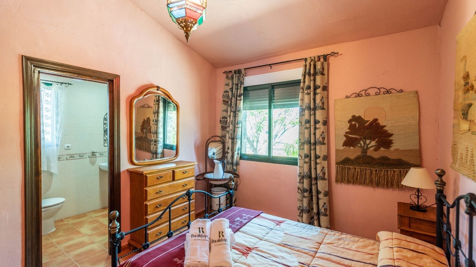 Un dormitorio con cama, cómoda, espejo, ventana con cortinas y un tapiz de pared.