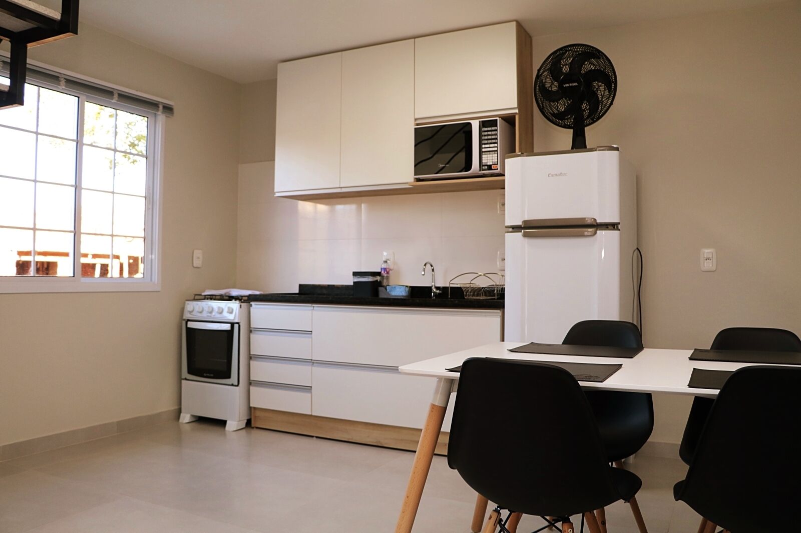 Una cucina moderna con mobili bianchi, un forno a microonde, un frigorifero e un tavolo con sedie.