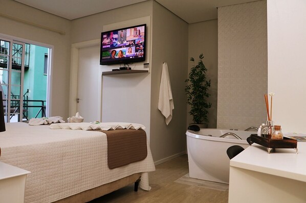 Ein Hotelzimmer mit einem Bett, einem an der Wand befestigten Fernseher, einer Badewanne und einer Pflanze.