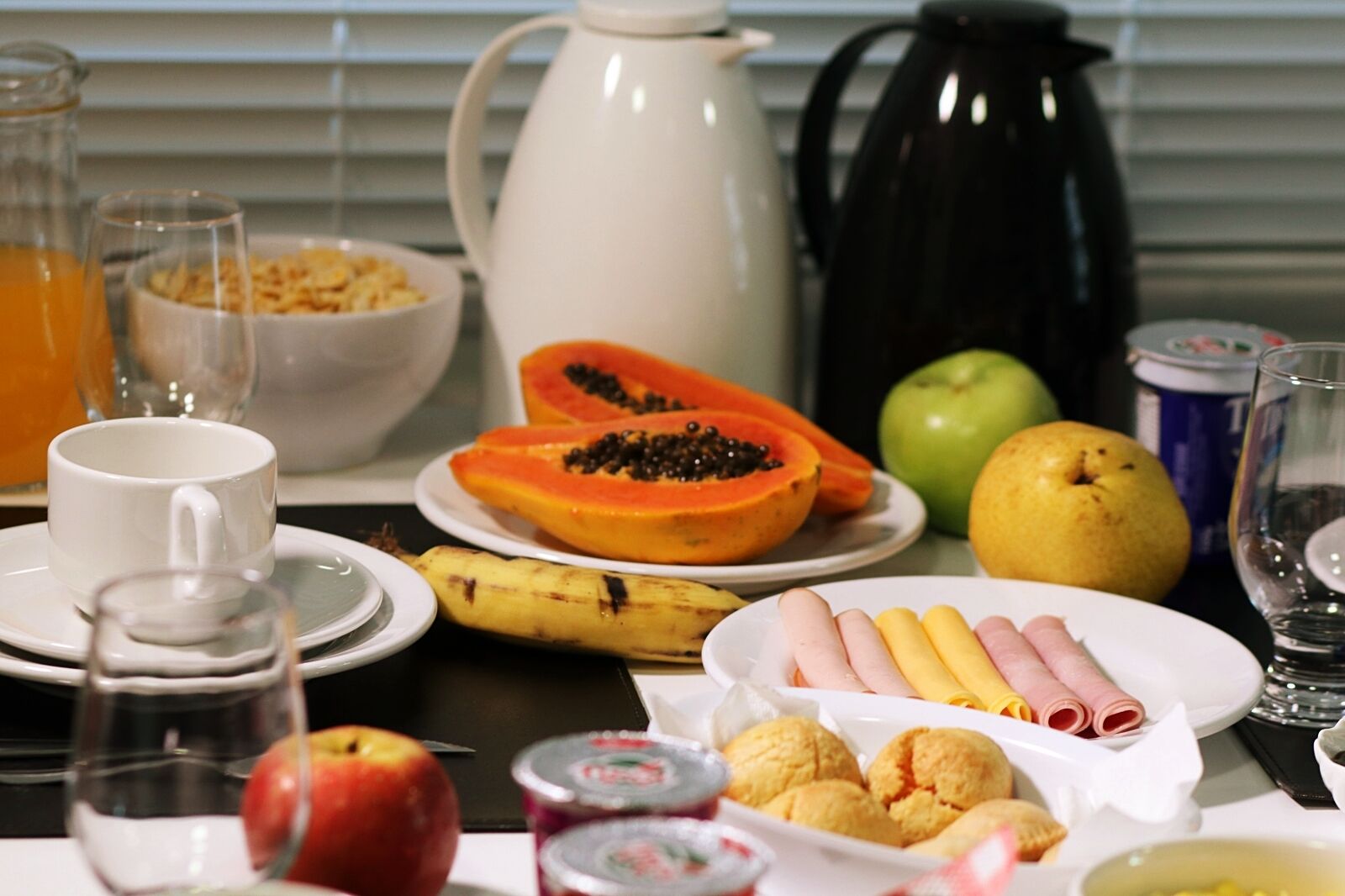Een ontbijttafel met diverse etenswaren, een koffiepot en een karaf sinaasappelsap.