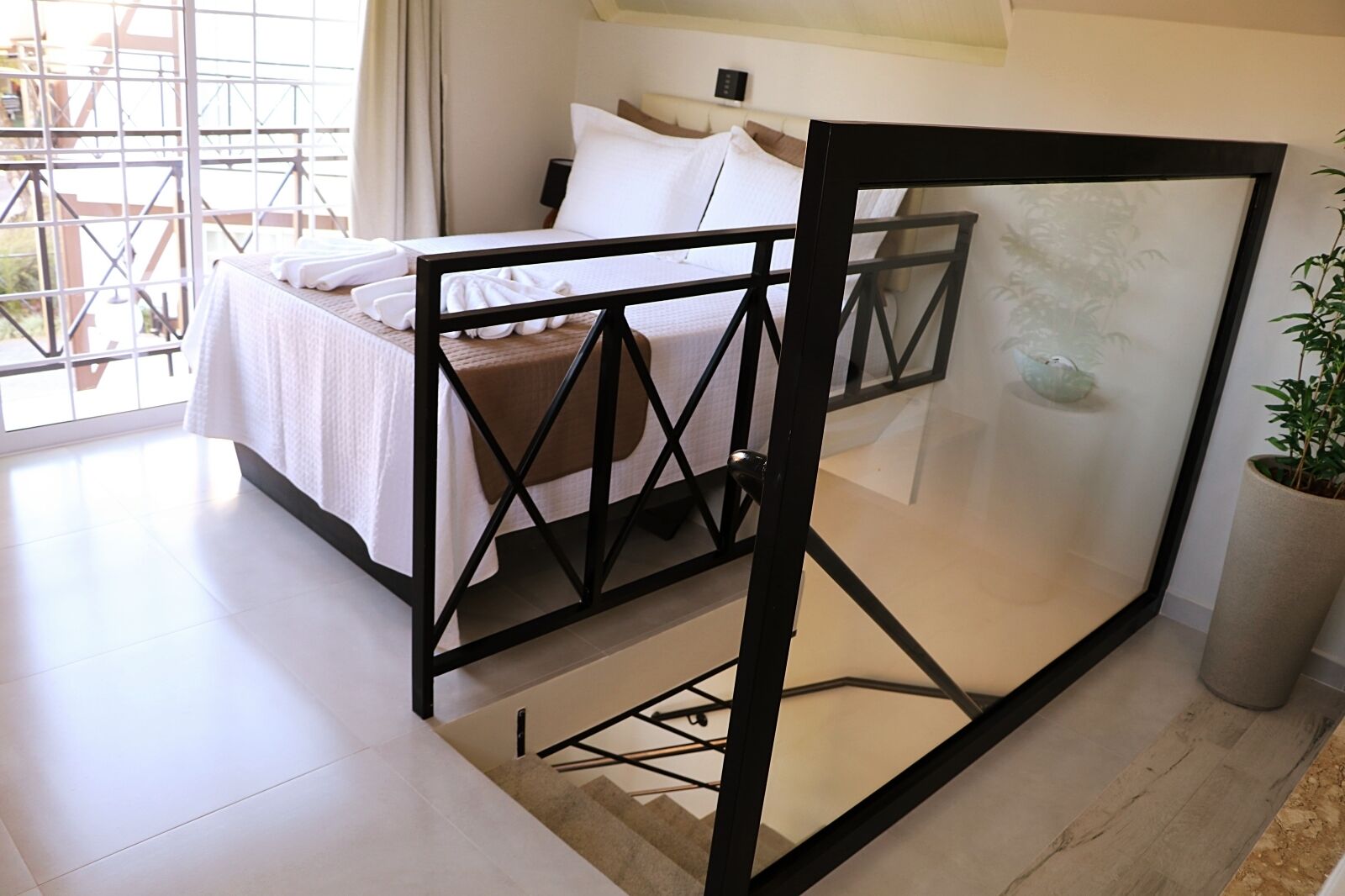 A modern bedroom with a bed, a large window, and a potted plant.