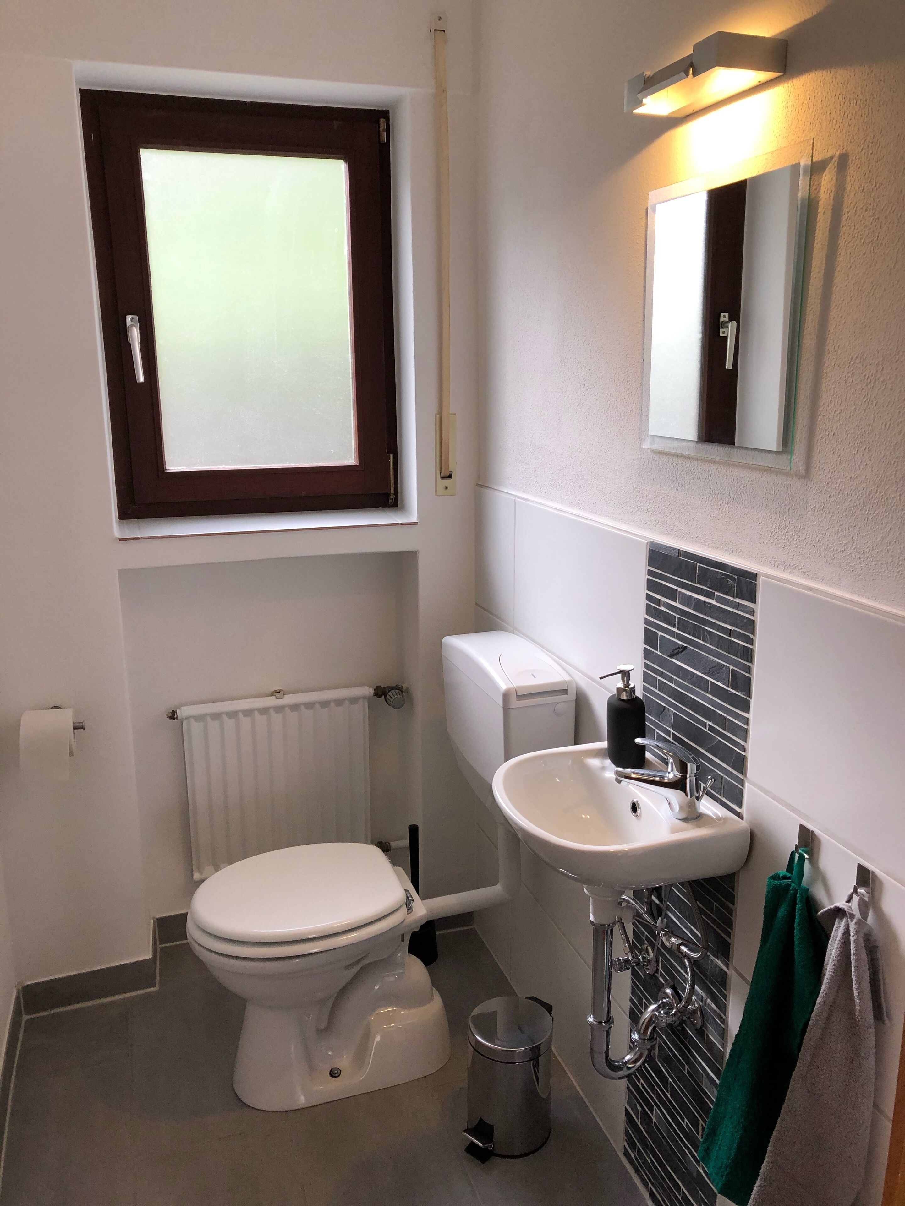 Une petite salle de bain comprenant des toilettes, un lavabo, un radiateur et une fenêtre.
