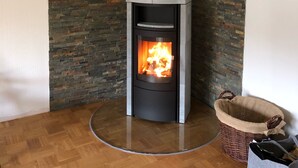 A modern wood-burning stove with a stone wall backdrop, a wooden floor, and a wicker basket. - Vacation home Buchfink 118sqm near Koblenz & Montabaur (Dies)