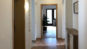 A hallway with wooden flooring, white walls, and a door on the left. There is a plant in the center and a small table on the right. - Vacation home Buchfink 118sqm near Koblenz & Montabaur (Dies)