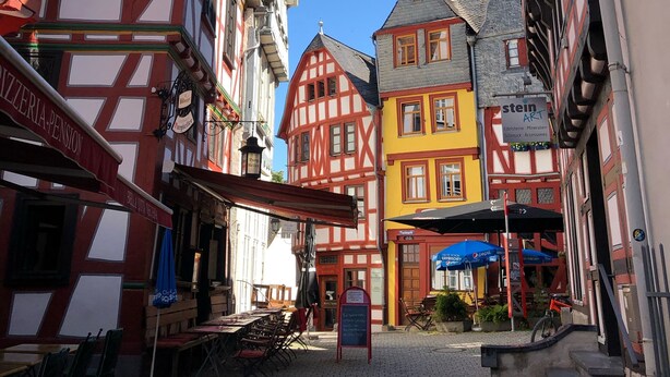 A cobblestone street with traditional half-timbered buildings, a café, and a sign for 'stein ART'. - Vacation home Buchfink 118sqm near Koblenz & Montabaur (Dies)
