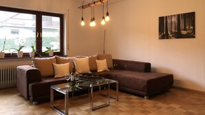 A living room with a brown sofa, a glass coffee table, and a painting on the wall. - Vacation home Buchfink 118sqm near Koblenz & Montabaur (Dies)
