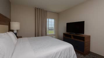 Una habitación de hotel con una cama, un televisor sobre un soporte de madera, una ventana con cortinas y una lámpara en una mesita de noche.