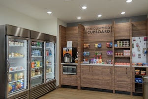 Una kitchenette con cafetera, microondas y refrigerador lleno de bebidas y aperitivos.