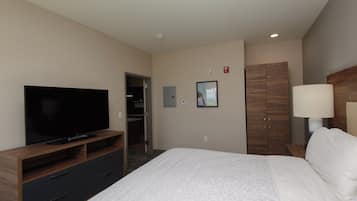 A hotel room with a flat-screen TV, a bed with a patterned bedspread, a wardrobe, and a bedside lamp.