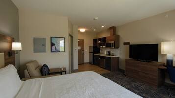 A hotel room with a large bed, a television, a kitchenette, and a bathroom.