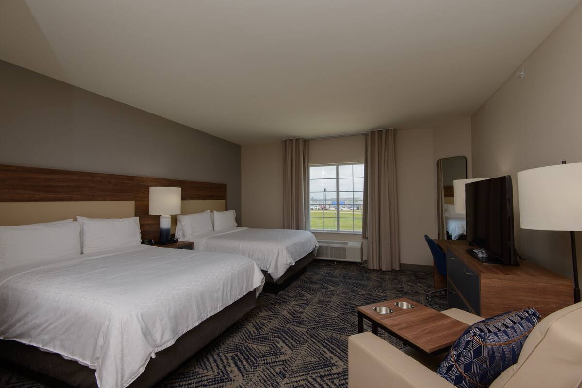 A hotel room with two beds, a desk, a chair, a TV, and a window with a view.