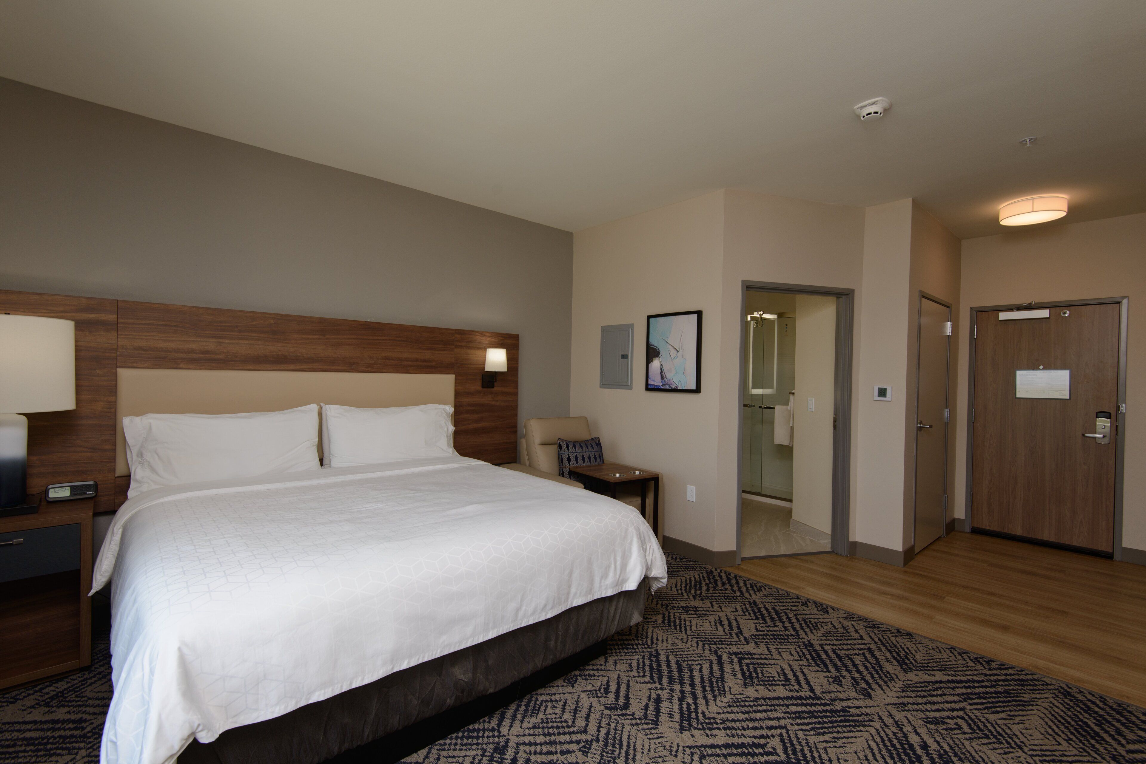 A hotel room with a large bed, bedside tables, a desk, a chair, a mirror, and a door.