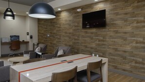 Una sala de reuniones moderna con una mesa larga, varias sillas, un televisor fijado a la pared y una pared de acento de madera.