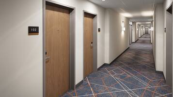 A hotel hallway with wooden doors, numbered signs, and patterned carpet.