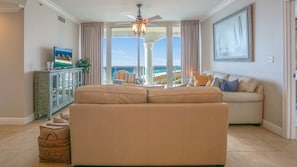 A living room with a beige sofa, a television, and a view of the ocean.