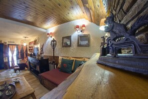Ein gemütliches Zimmer mit Holzboden, einem Kamin, einer Couch mit Karokissen und einer dekorativen Wandleuchte.