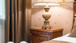 Een net opgemaakt bed met een gevouwen handdoek, een bedlampje en een houten nachtkastje met lade.