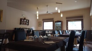 Un comedor con mesas dispuestas para el servicio, un ventilador de techo y un ventanal que proporciona luz natural.