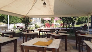 Un patio al aire libre con mesas y sillas, una zona cubierta y vista a un edificio al fondo.