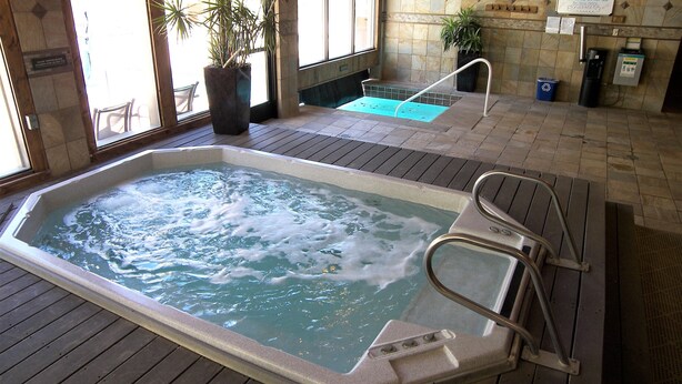 Een hottub met een houten terras, een plant in een pot, een klein zwembad en een bord aan de muur.