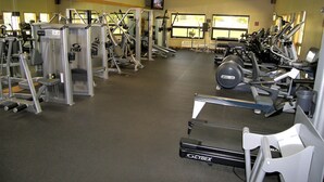 Een sportschool met diverse fitnessapparaten, spiegels en een televisie aan de muur.