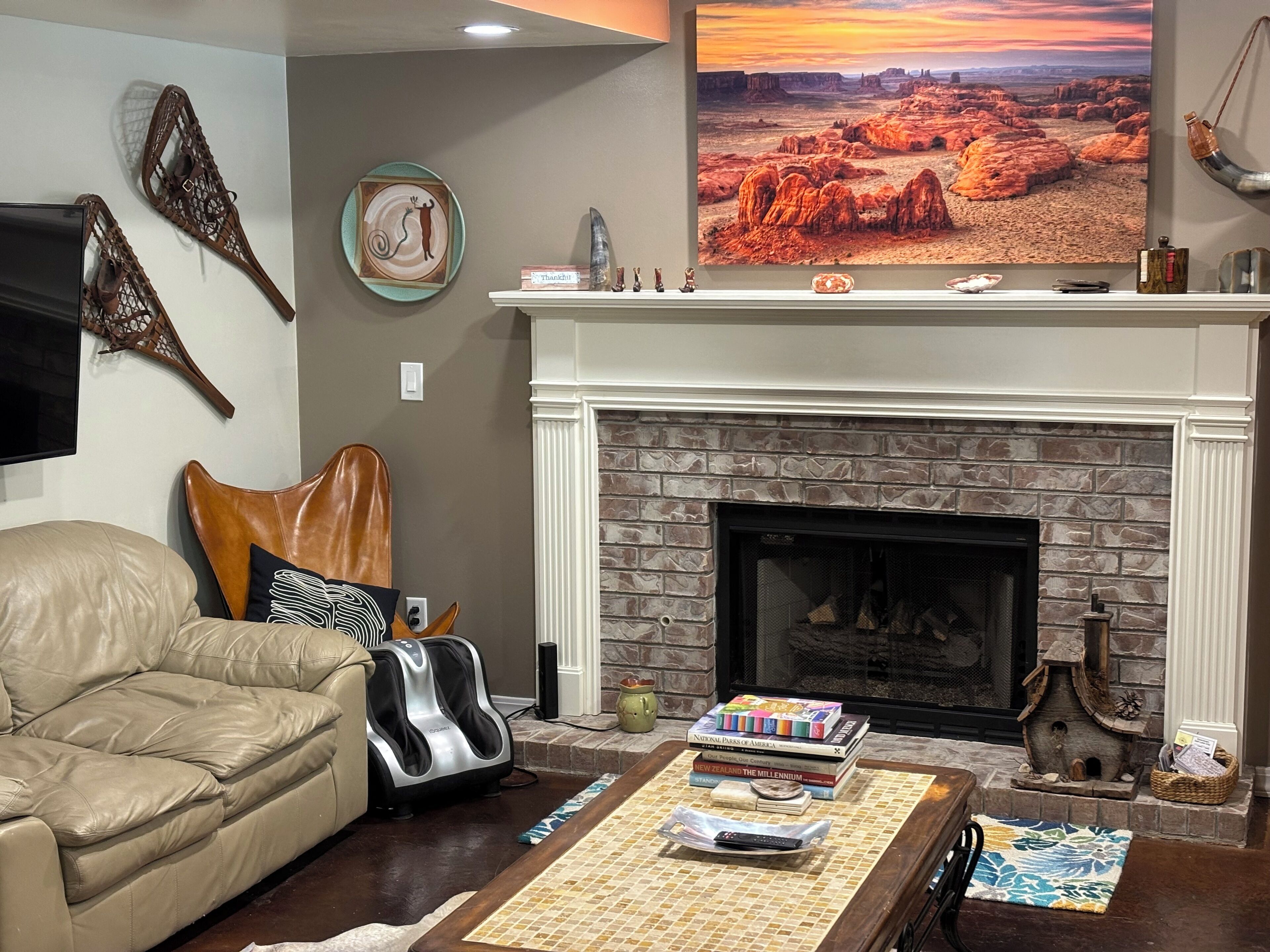 A living room with a stone fireplace, leather sofa, and a mounted TV.
