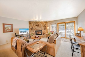 A cozy living room with a stone fireplace, a television, and a dining area with a table and chairs.