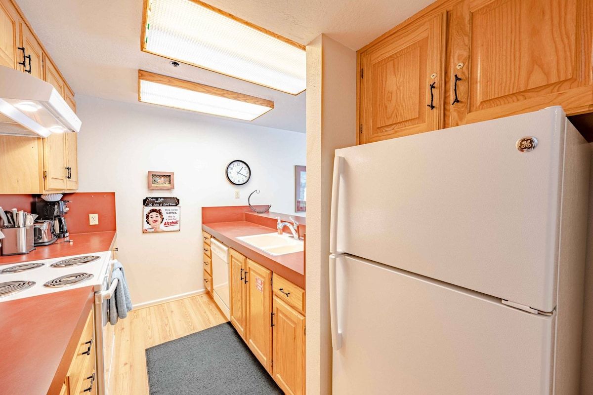 A compact kitchen with wooden cabinets, a white refrigerator, a stove, and a sink.