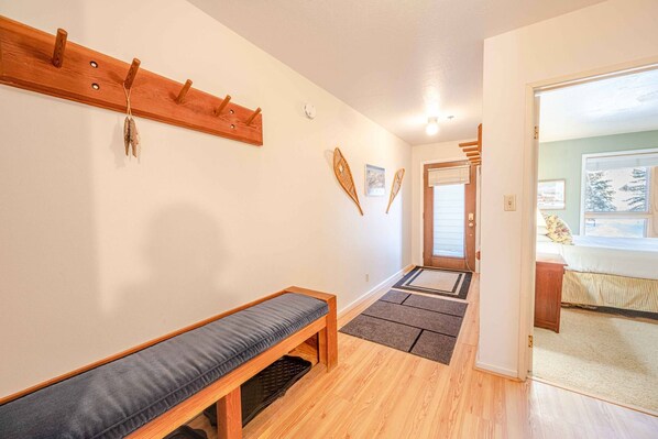 Un pasillo con un banco, perchero y una puerta que da a otra habitación.