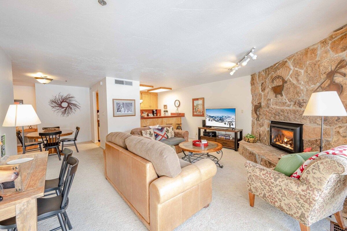 Una sala de estar con sofá, un sillón estampado, chimenea y televisión.