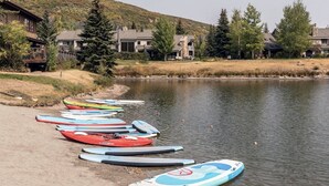 A lakeside view with paddleboards lined up on the shore, surrounded by residential buildings and trees.