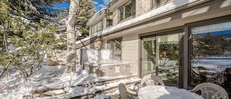 Un espacio exterior cubierto de nieve con un jacuzzi, una mesa de patio y sillas.