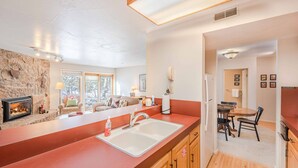 A modern kitchen with a stone wall, a built-in fireplace, a large island with a sink, wooden cabinets, and a dining area with a table and chairs.