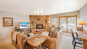 A cozy living room with a stone fireplace, a television, and a dining area with a table and chairs.