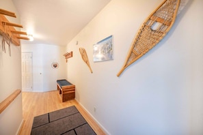 A hallway with a wooden bench, a door, and wall-mounted decorations including a framed picture and a woven basket.