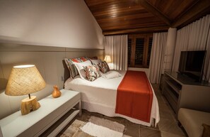 Ein modernes Schlafzimmer mit einem großen Bett, einem Nachttisch mit Lampe, einem Fernseher und einem Fenster mit Vorhängen.