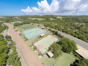 Ein großer Sportkomplex mit mehreren Tennisplätzen, umgeben von Grünflächen und einer Straße.