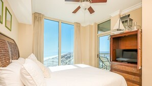 Ein Hotelzimmer mit einem großen Bett, einem Deckenventilator, einem Fernseher und Blick auf den Strand.