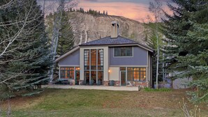 Une maison moderne à deux étages, dotée de grandes fenêtres, d’une cheminée et offrant une vue sur les montagnes.