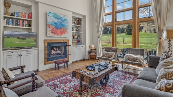 A living room with a fireplace, bookshelves, a television, and a view of a golf course.