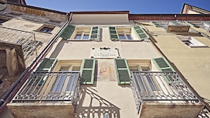 A building with a sign indicating it is a historical site, balconies with green shutters, and a clear sky. - Dora maison de charme (Ivrea)