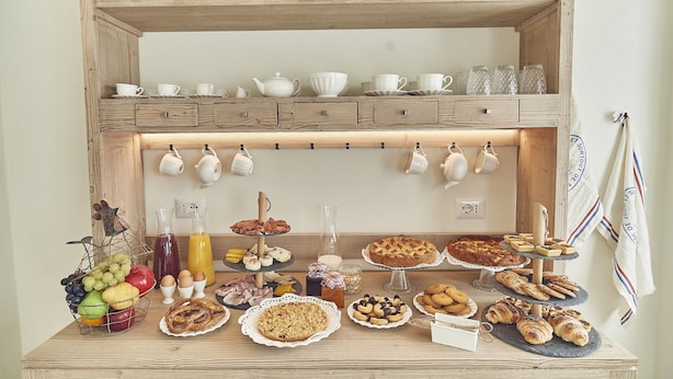 A breakfast buffet with various food items and a selection of white cups and teapots on shelves. - Dora maison de charme (Ivrea)