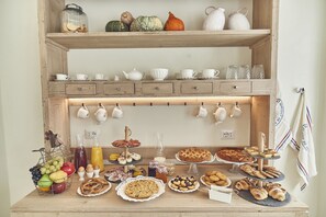 A breakfast buffet with various food items and a selection of white cups and teapots on shelves. - Dora maison de charme (Ivrea)