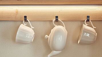 Three white ceramic mugs hanging on a wooden shelf.
