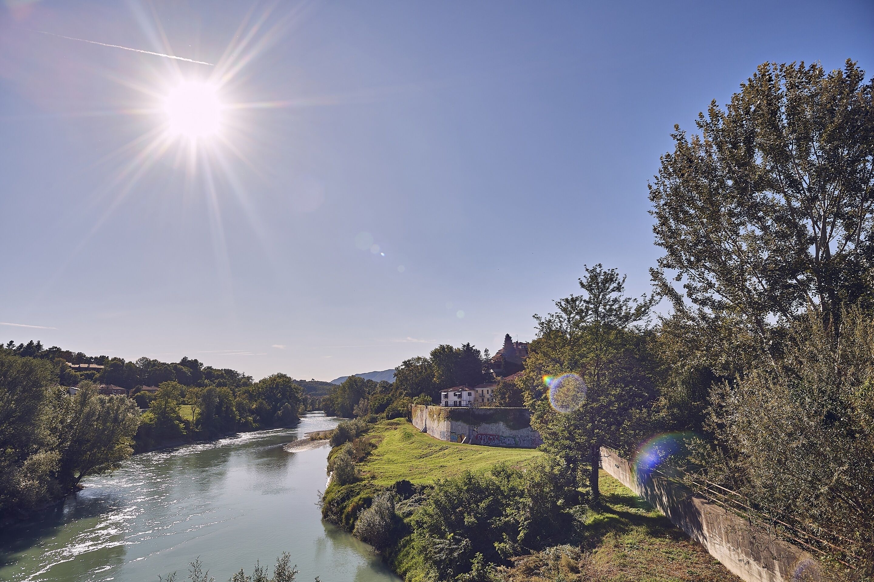 A river with a bridge, a house on a hill, and a clear sky.