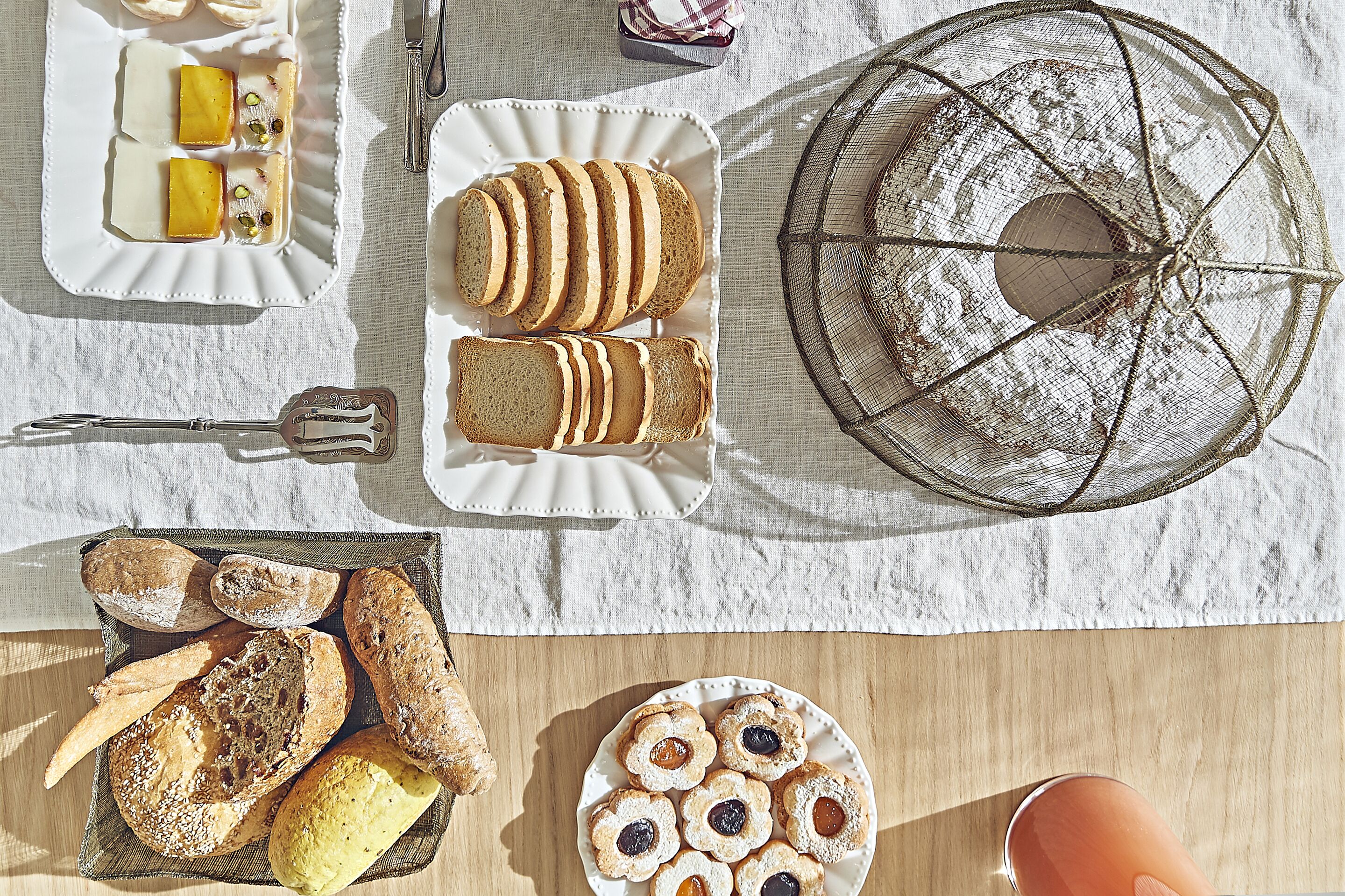A table with various breads and pastries, a cake, and a basket of bread.