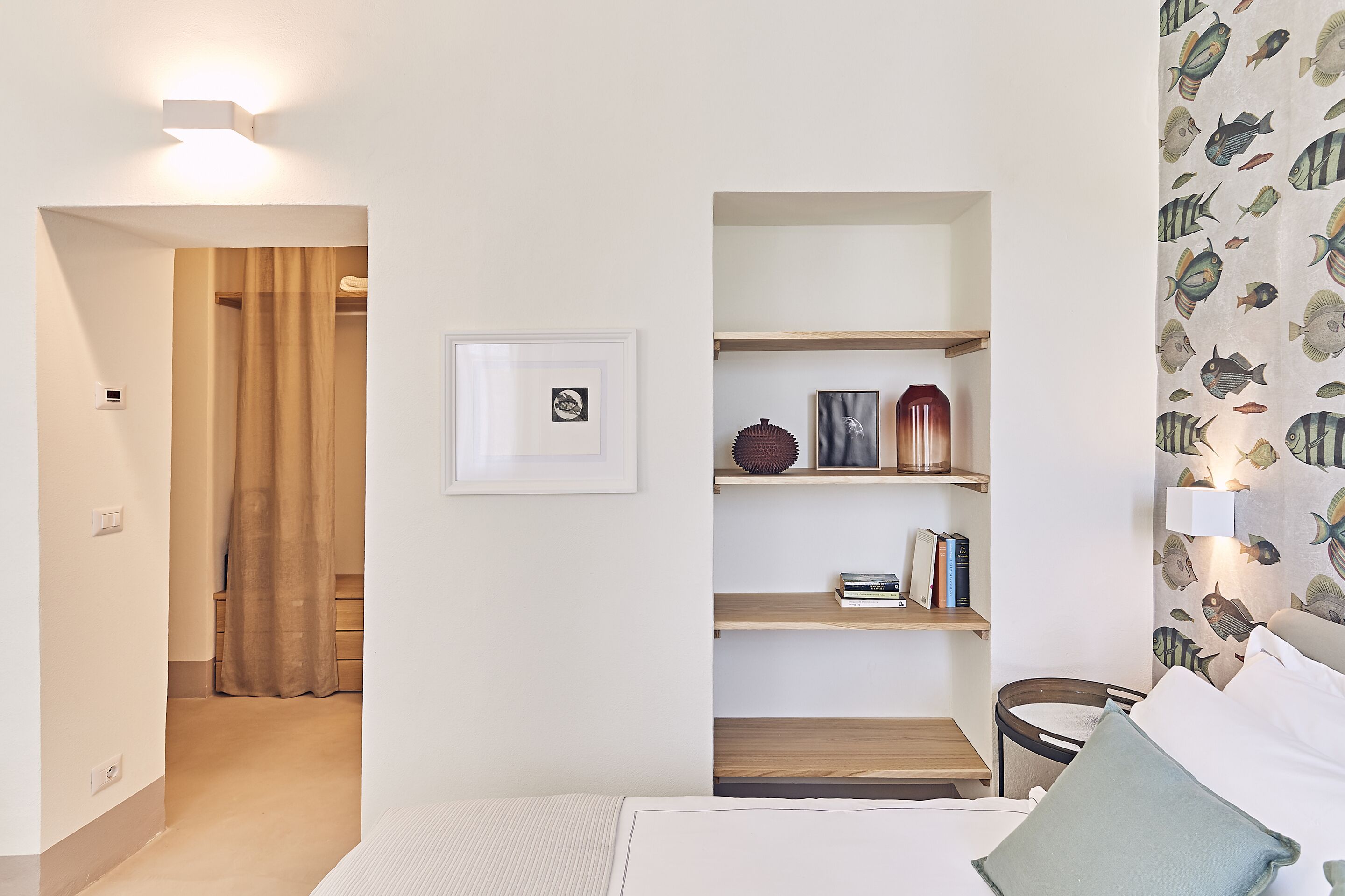Una camera da letto moderna con un letto, un comodino, una mensola con dei libri, un quadro incorniciato e una tenda.