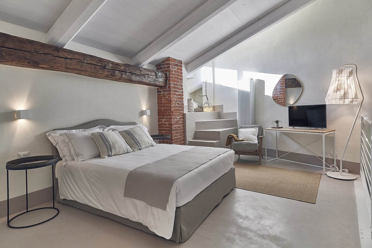 A modern bedroom with a large bed, a desk with a TV, and a chair.